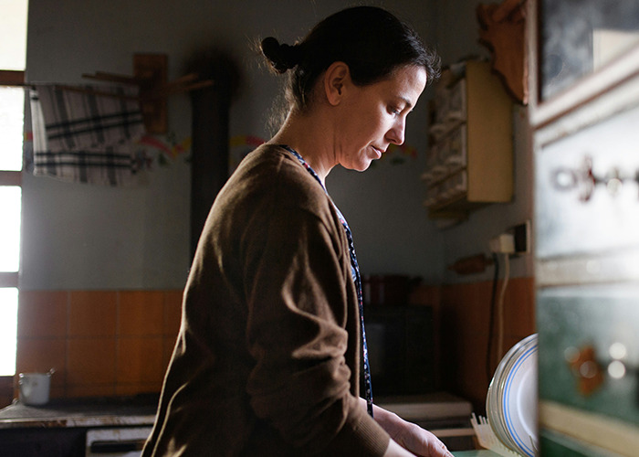 Woman in kitchen thoughtfully washing dishes, reflecting on benefits of marriage for women, natural light highlighting her profile.