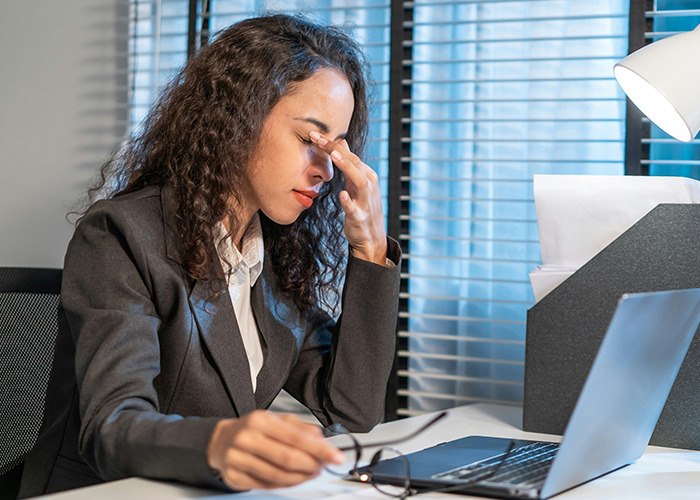 Woman in business attire sitting at desk with laptop, rubbing her eyes, reflecting on benefits of marriage for women.