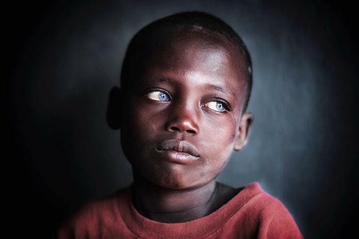 Portrait of a child with blue eyes wearing a red shirt, showcasing beautiful childhood moments around the world.