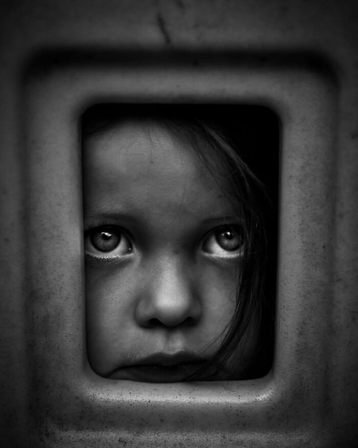 Close-up black and white photo of a child's face framed by a square opening, capturing childhood emotions worldwide.