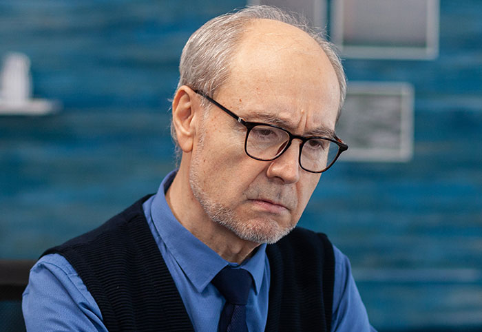 Elderly businessman with glasses in an office, looking concerned about a lost big client due to an easily replaceable employee