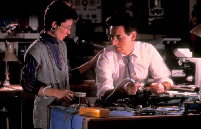Two people working with electronic equipment in a dimly lit room, illustrating unrealistic women movie tropes.