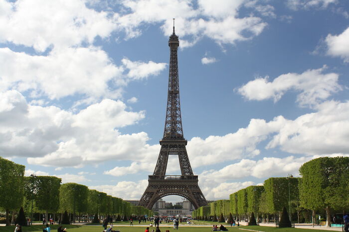 Eiffel Tower under a partly cloudy sky with visitors on the grass, illustrating funny events from history.