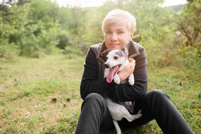 Elderly lady sitting outdoors hugging a happy dog, illustrating a story about allegedly planning to steal neighbor&rsquo;s doggo.