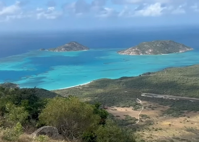 Aerial view of Great Barrier Reef island with turquoise waters and green vegetation under a partly cloudy sky.