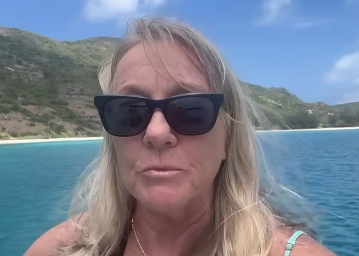 Elderly woman wearing sunglasses on a boat with Great Barrier Reef island landscape in the background.