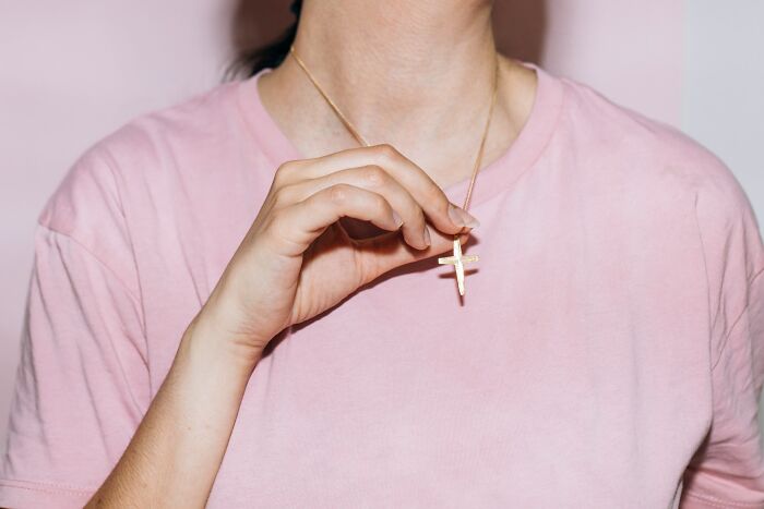 Person wearing a pink shirt holding a gold cross necklace symbolizing chaotic breakup stories from exes in emotional moments.