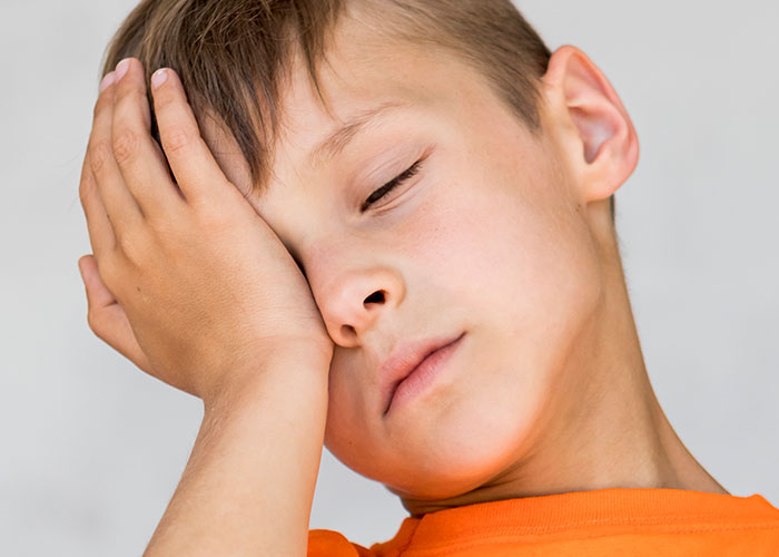 Young boy in an orange shirt looking embarrassed and covering part of his face, reflecting childhood cringe moments.
