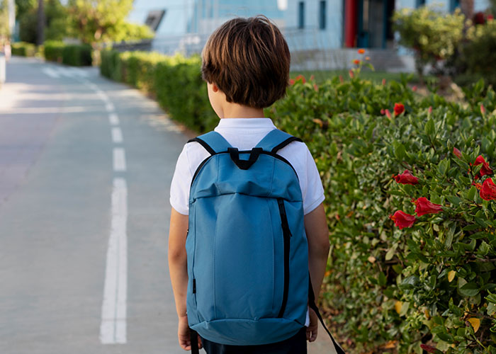 Child with blue backpack walking outdoors, evoking memories of things people did as kids that make them cringe.