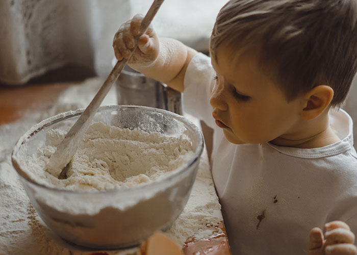 Young child mixing flour in a bowl, a nostalgic moment reflecting childhood things people did that make them cringe today.