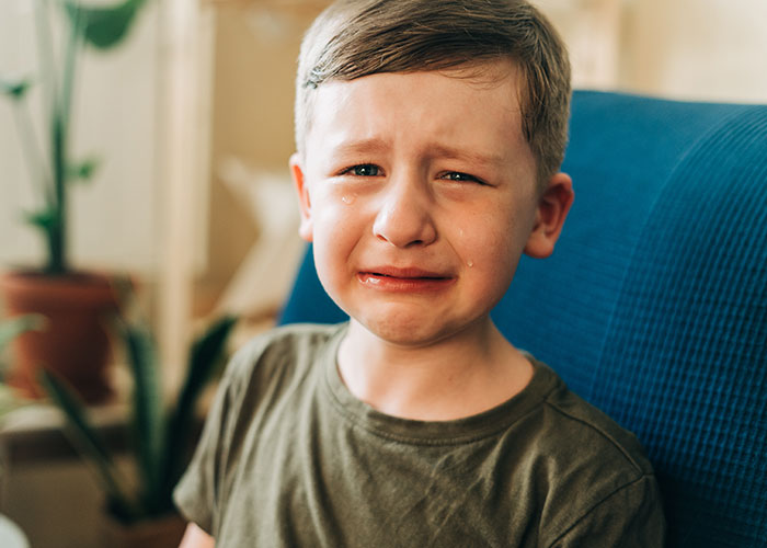 Young boy crying on a chair, representing childhood moments that make people cringe when recalling things they did as kids.