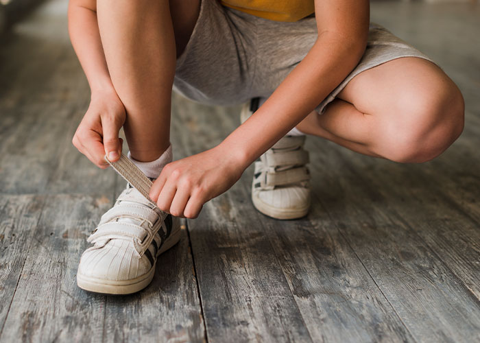 Child crouching on wooden floor tying shoelaces, reflecting on childhood moments that make them cringe today.
