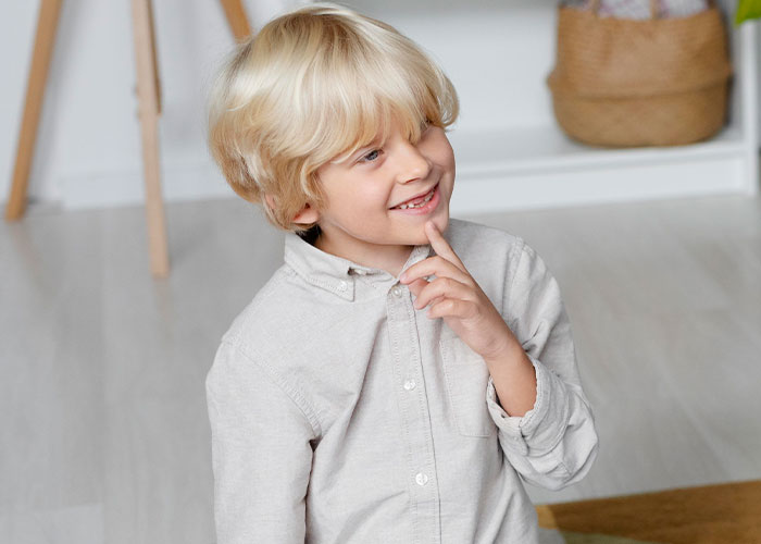 Blond boy smiling thoughtfully indoors, reflecting on childhood memories that make him cringe today.