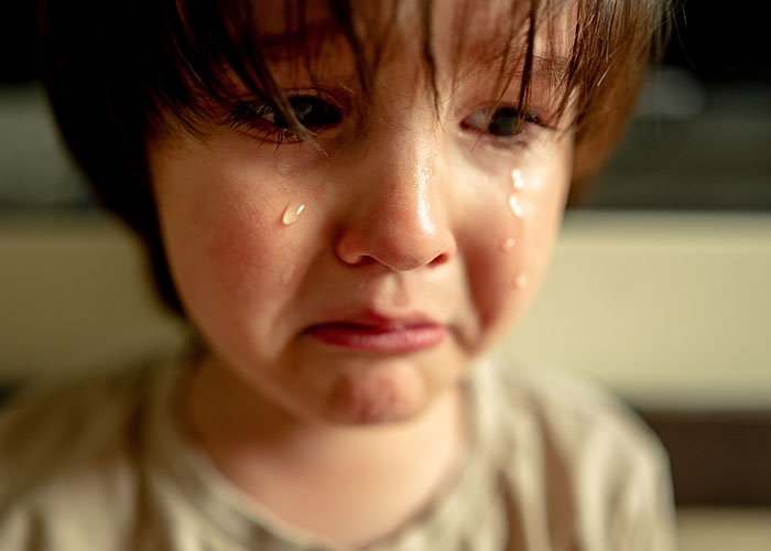 Close-up of a young child crying with tears streaming down the face, reflecting childhood cringe moments.