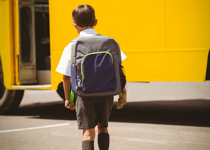 Young boy with backpack walking toward a yellow school bus, reflecting on childhood things that make them cringe.