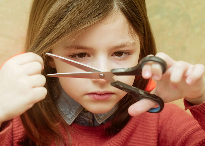 Young girl focused on cutting her hair with scissors, reflecting on childhood things people did that make them cringe today.