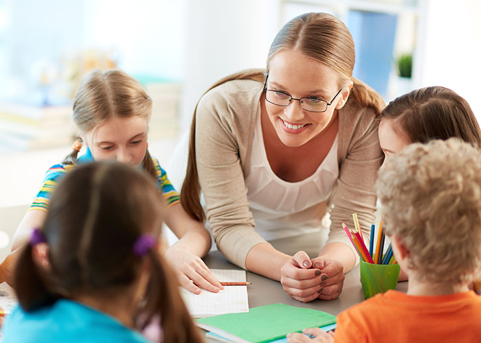 Teacher smiling and interacting with children during a classroom activity about things people did as kids that make them cringe