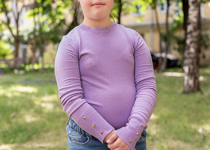 Young child wearing a purple long-sleeve shirt standing outdoors, reflecting on childhood cringe moments.