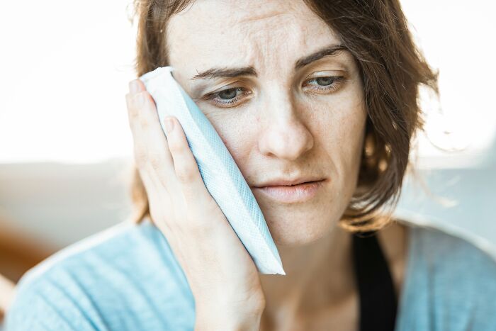 Woman holding ice pack to her face, showing pain and distress from medical neglect effects today.