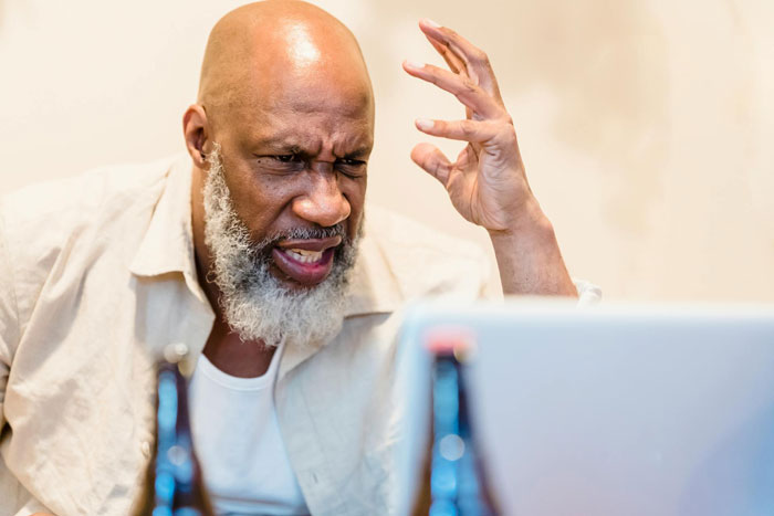 Frustrated man with a beard reacting angrily while looking at a laptop during a house ride discussion.
