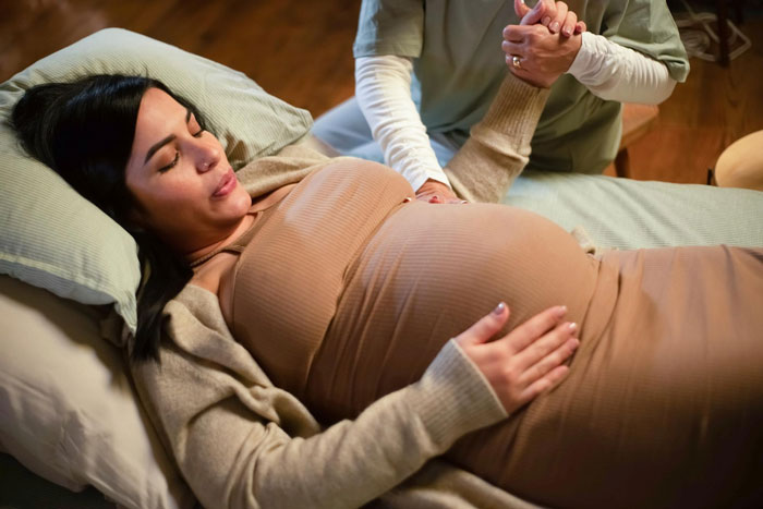 Pregnant woman in labor holding hands with support person, highlighting ex arguing while girlfriend is in labor.