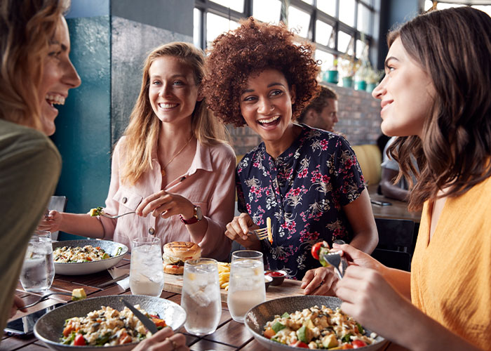 Group of women enjoying dinner together at a restaurant, highlighting friend group dynamics and social invitations.