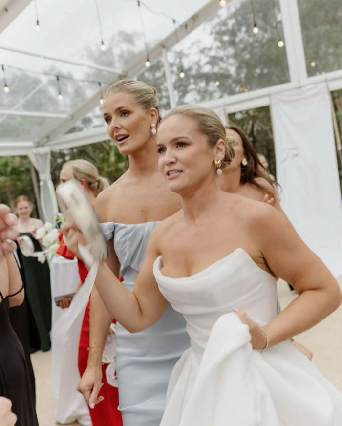 Bride and bridesmaid at a wedding in a tent, showing emotion during photos by a well-known professional photographer.