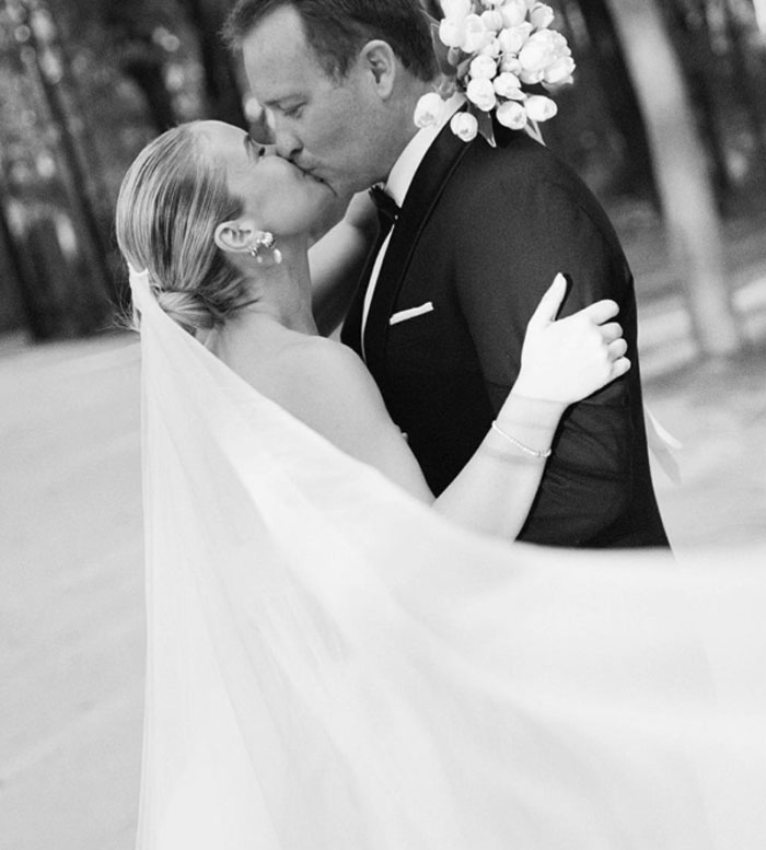 Bride and groom sharing a kiss during wedding photoshoot captured by a professional photographer outdoors in black and white.