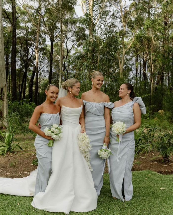 Bride and bridesmaids dressed in elegant gowns posing outdoors for professional wedding pics in a natural forest setting.