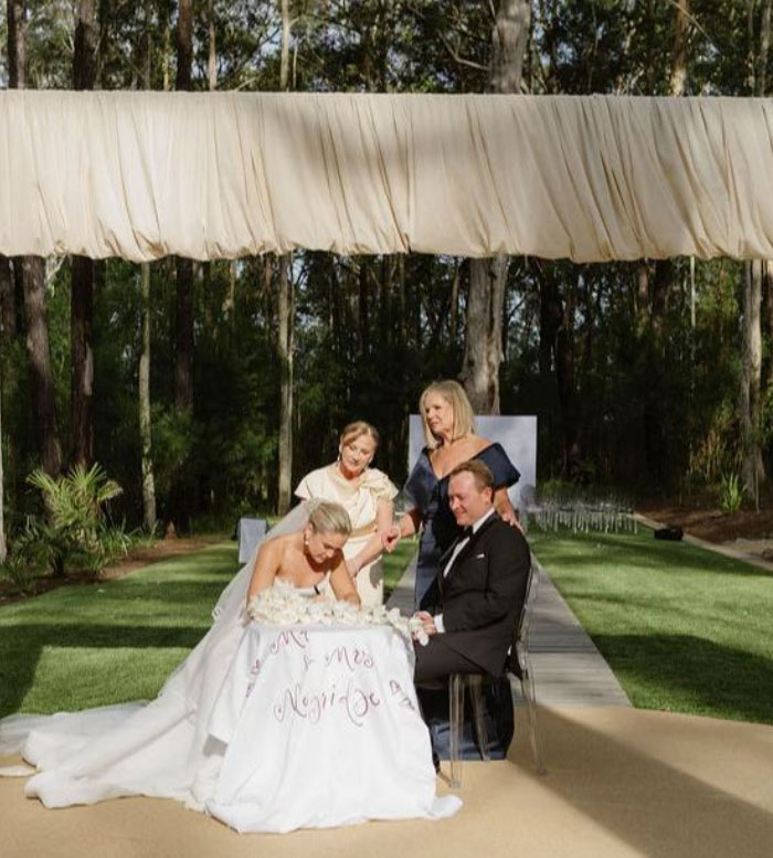 Bride and groom with two women at outdoor wedding ceremony, capturing wedding pics in natural forest setting.