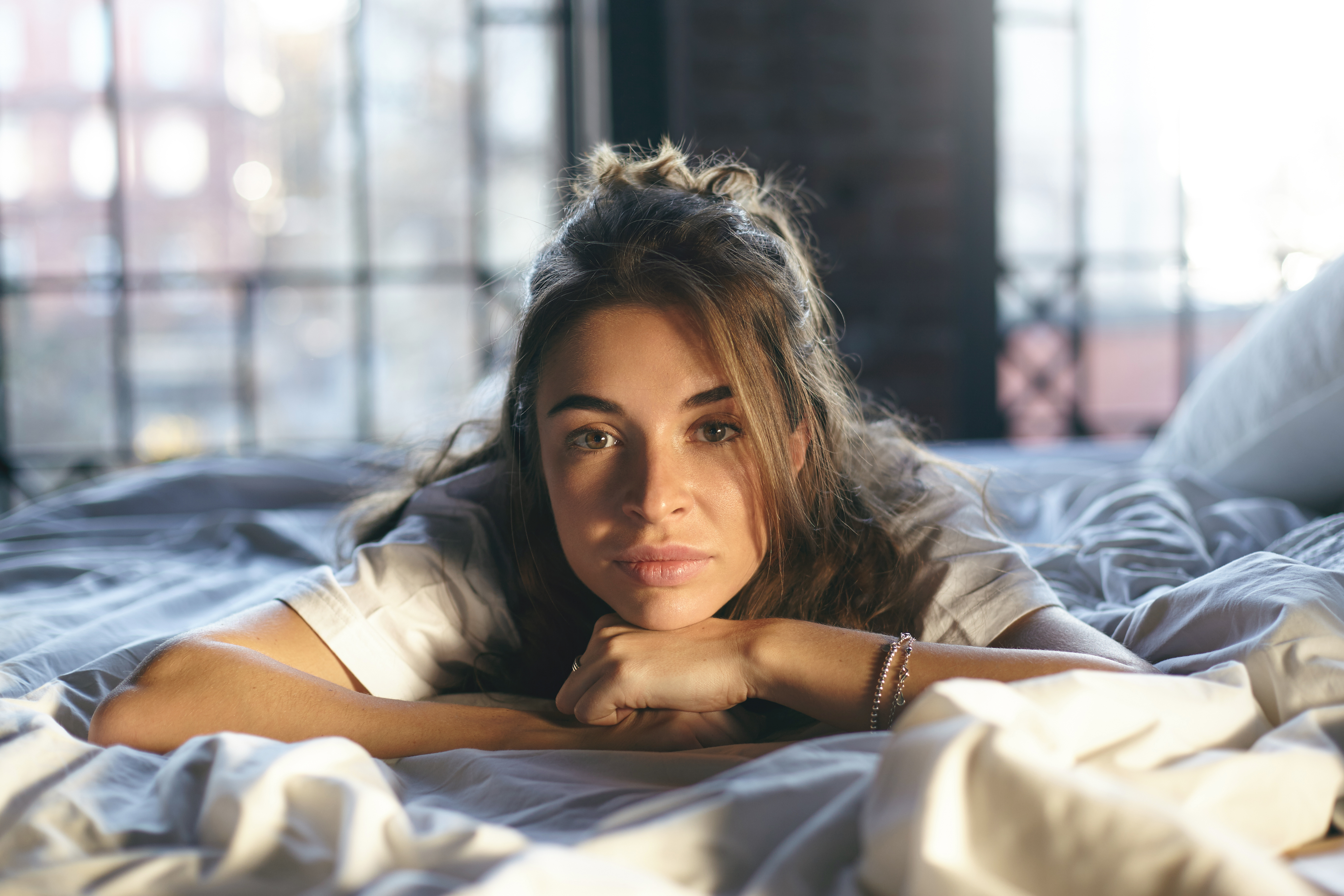 Young woman with natural skin and messy hair lying on bed, reflecting on her long beauty routine and shaving.