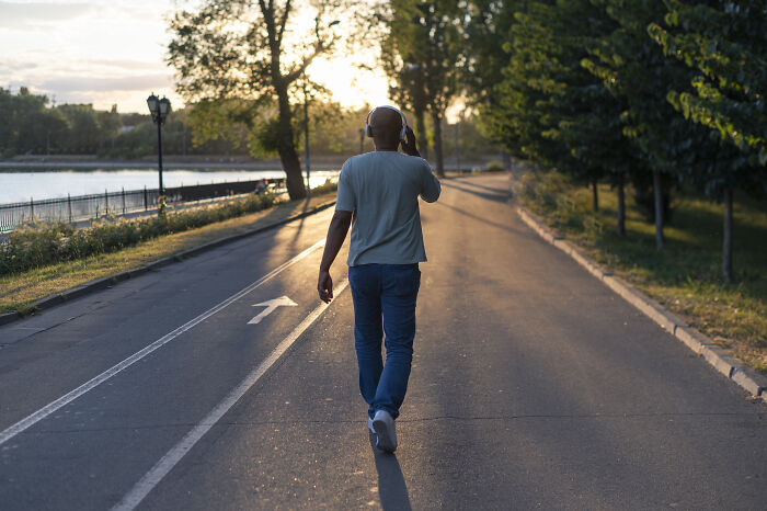 Man walking on a tree-lined path at sunset, wearing headphones and casual clothes, exploring loopholes advantage.