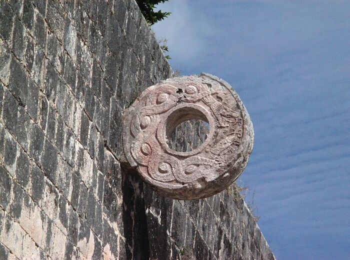 Ancient carved stone ring on a wall likely used in dangerous historical sports in a clear outdoor setting.