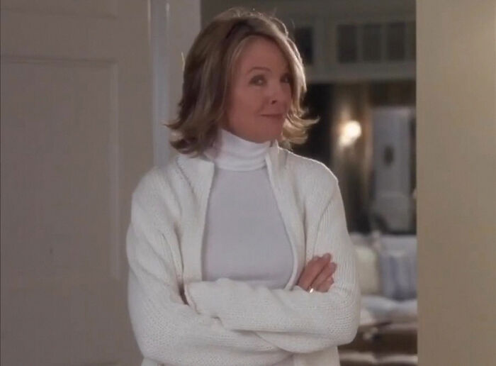 Woman in a white turtleneck and sweater standing indoors, related to Diane Keaton cause revealed after unexpected passing.