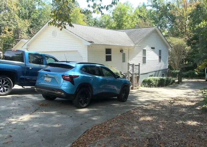 Driveway of a house with parked cars, associated with sister&rsquo;s emotional reaction after brother found alive in basement.