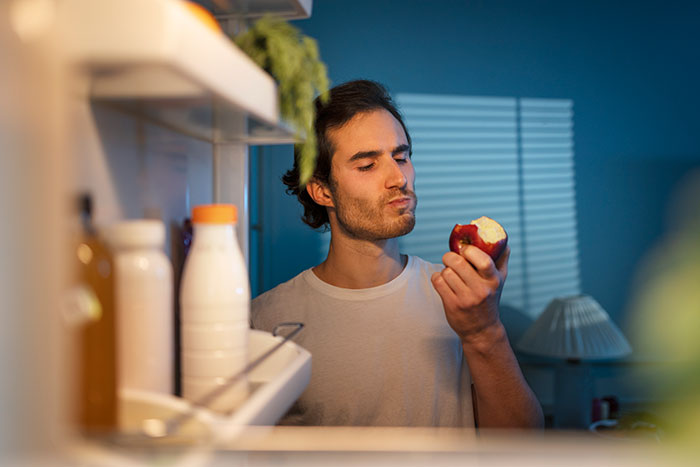 Young man eating an apple in a kitchen late at night, illustrating a friend who ate everything owned by the hosts. Young man eating an apple in a kitchen late at night, illustrating a friend who ate everything owned by the hosts.