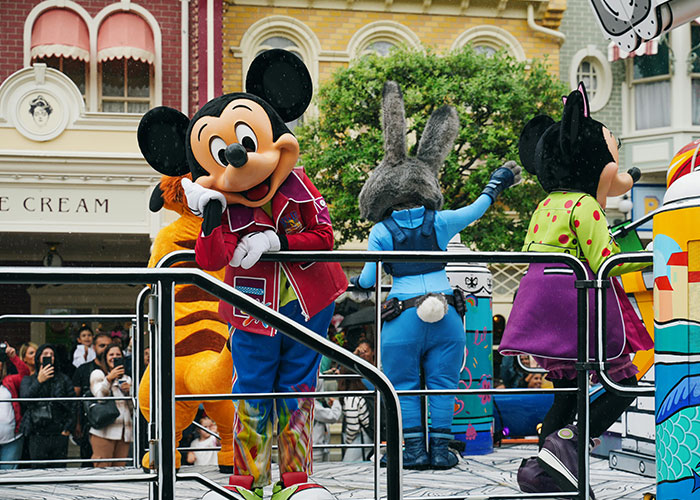 Family enjoying separate drive at Disneyland parade with Mickey Mouse and other characters entertaining the crowd.