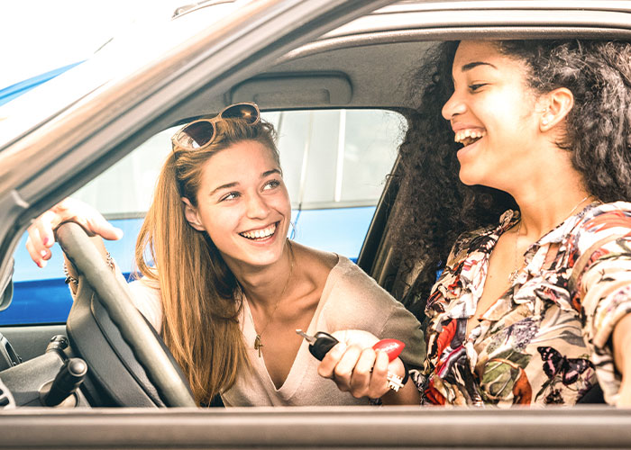 Two women smiling inside a car, one holding car keys, reflecting a family separate drive to Disneyland experience.