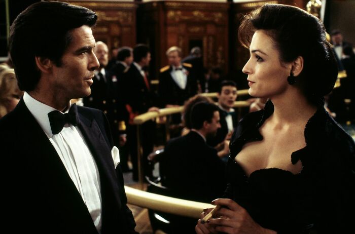 Man in tuxedo and woman in elegant dress talking at a formal event depicting unrealistic women movie tropes in cinema.