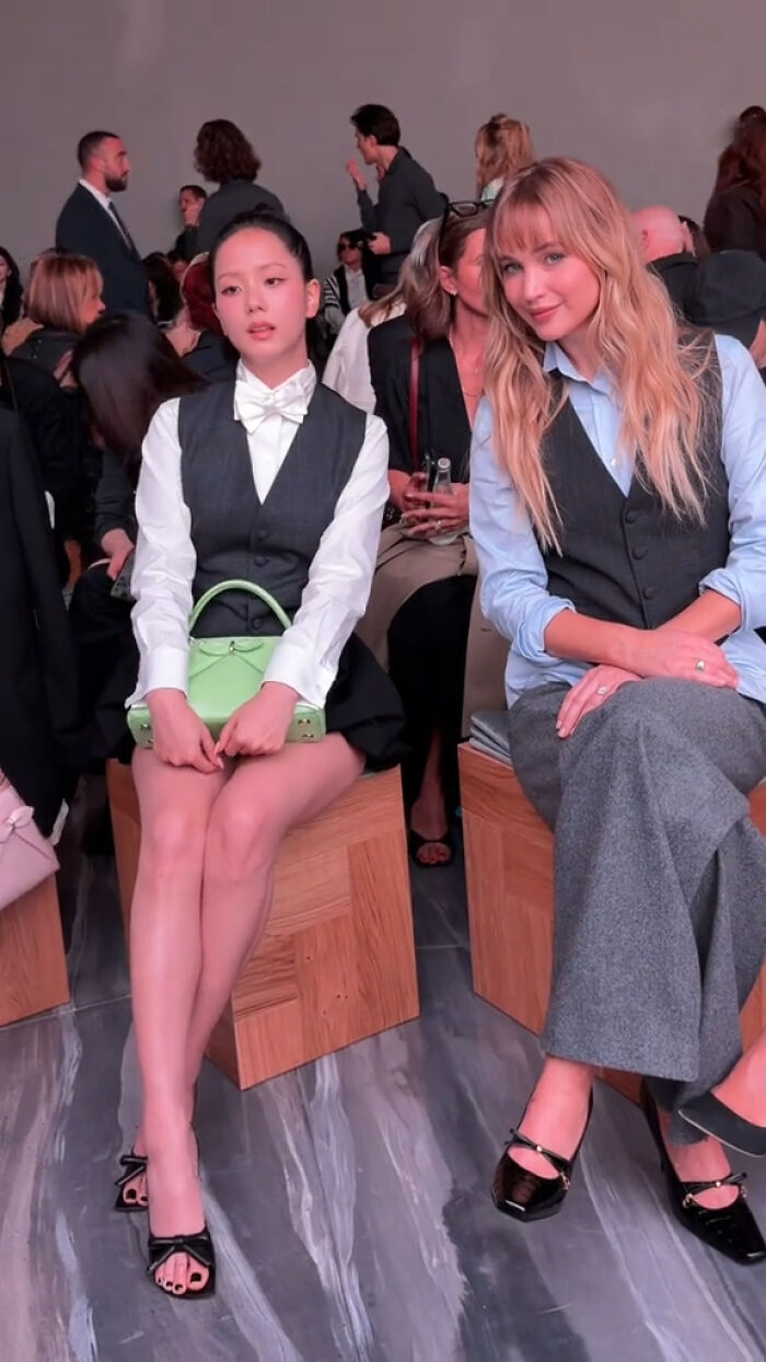 Two women sitting at Paris Fashion Week event, dressed stylishly, capturing the buzz around plastic surgeon arrests in LA.