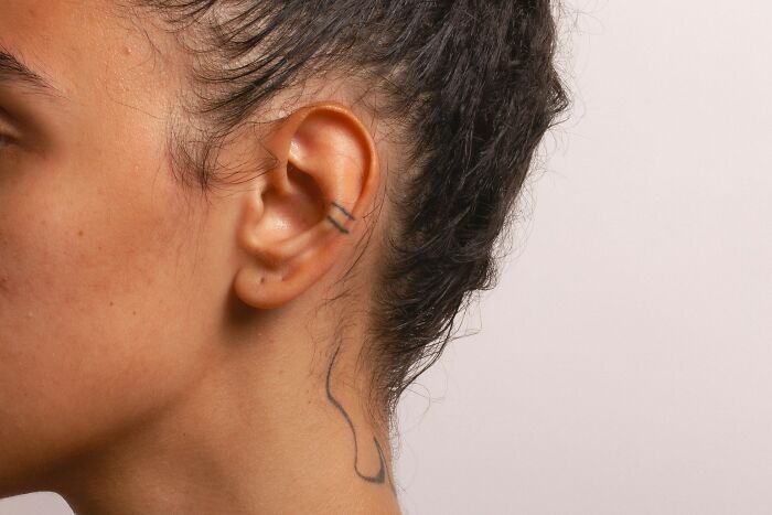 Close-up of a person’s ear and neck showing simple tattoos, illustrating unusual health hacks shared by patients.
