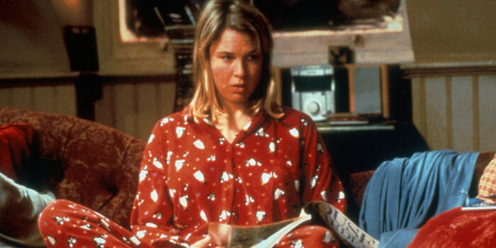 Woman in red pajamas sitting on a couch looking concerned, illustrating unrealistic women movie tropes in film scenes.