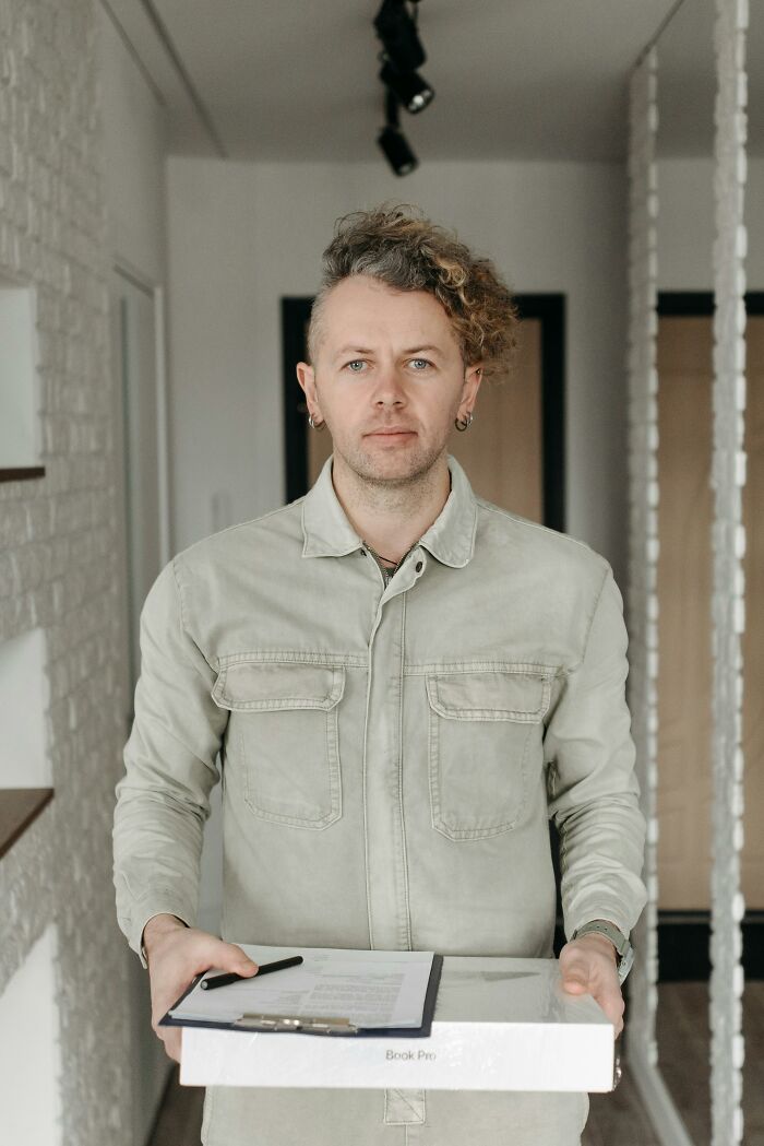 Person with curly hair holding a box and clipboard indoors, representing home protection and ways to outsmart burglars.