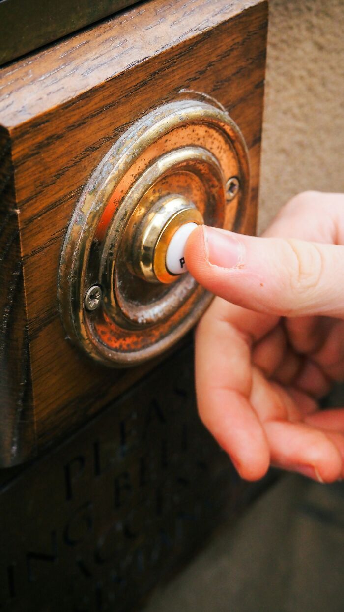 Hand pressing an old doorbell button on a wooden panel demonstrating ways to outsmart burglars and protect your home