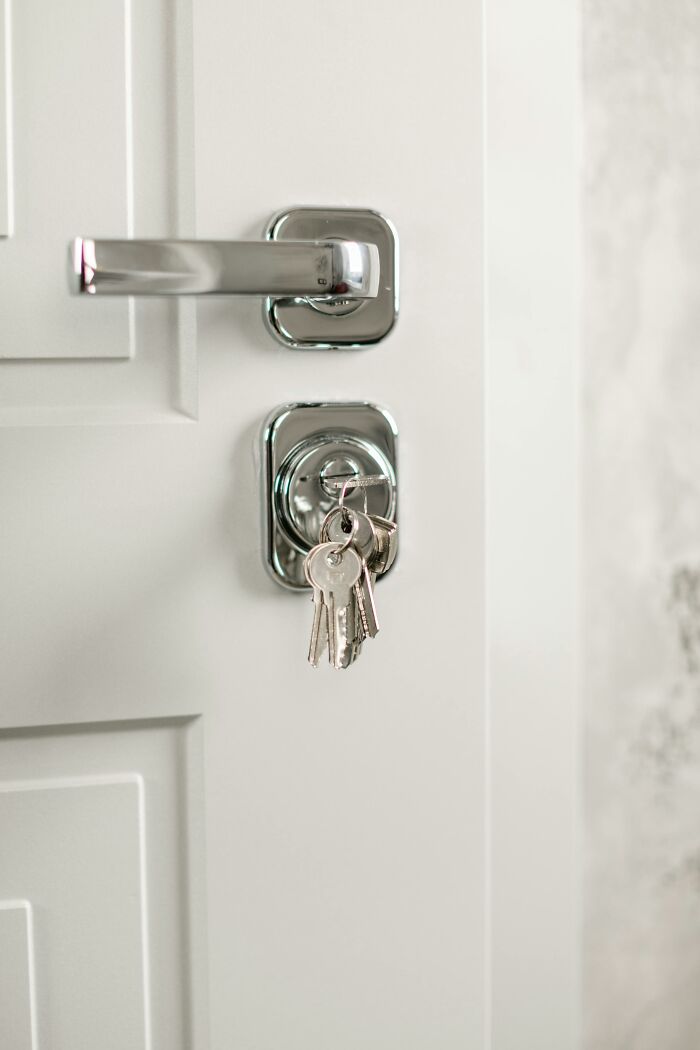 Silver keys hanging from a lock on a white door, illustrating easy ways to outsmart burglars and protect your home.