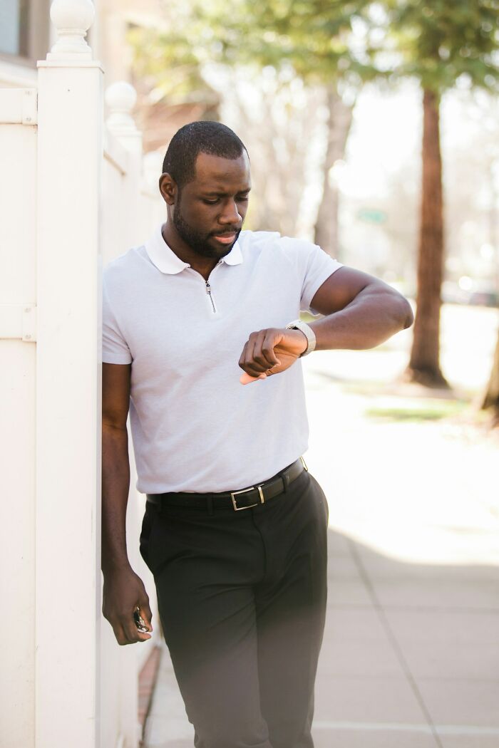Man in white shirt and black pants leaning on wall outdoors, checking his watch, reflecting on red flags ignored after wedding.