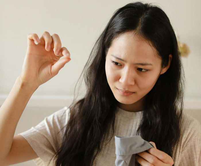Woman holding a strand of hair while cleaning the house, discovering evidence of a serial cheater caught red-handed.