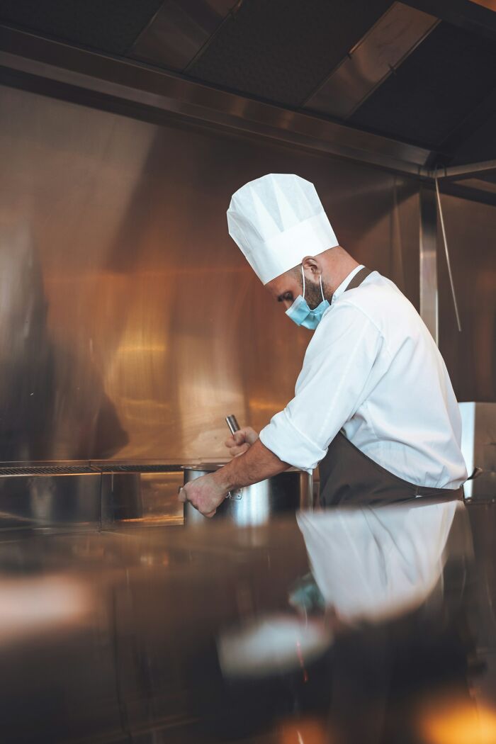 Chef disappointed in someone they idolized cooking in a commercial kitchen wearing a white hat and face mask.
