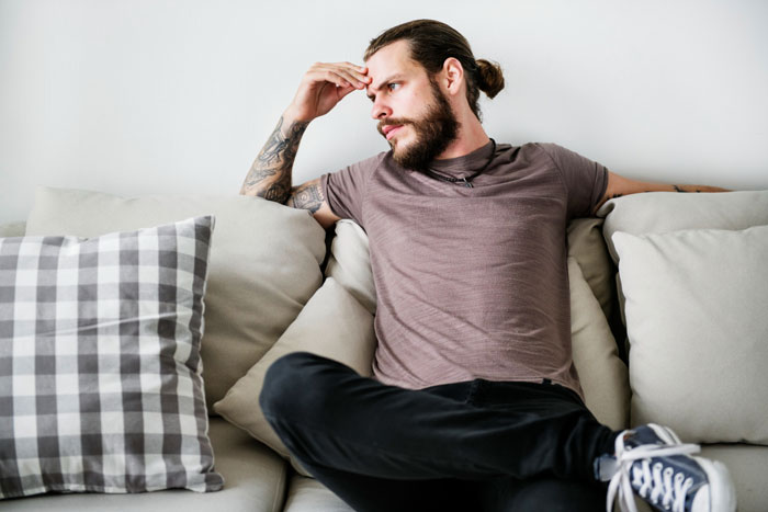 Man sitting on sofa looking frustrated, representing husband sick of hosting wife's distant relatives without thanks.