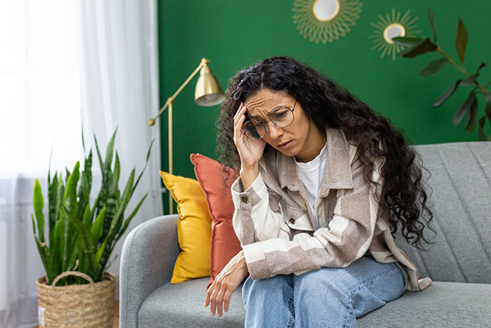 Woman sitting on couch looking stressed and upset after realizing she got duped by a friend who forgot her wallet.